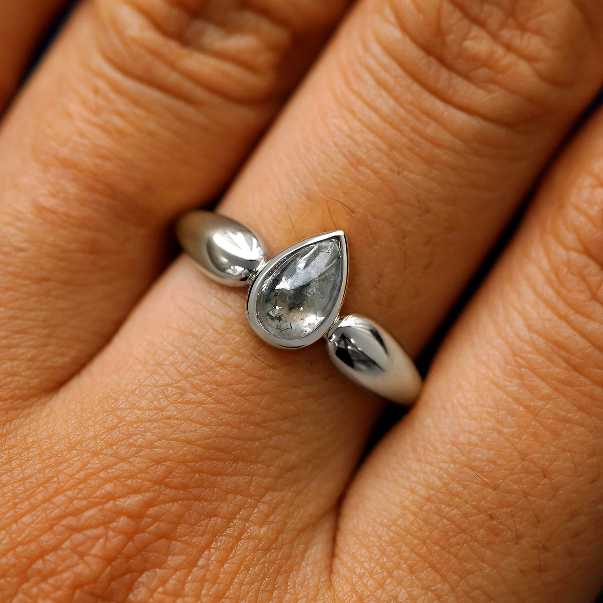 Close up view of a model's hand wearing a 950 platinum pear cabochon salt and pepper diamond engagement ring