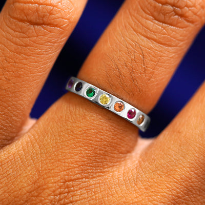 A platinum ring with an emerald, ruby, champagne and black diamonds, and sapphires of multiple colors in rainbow order