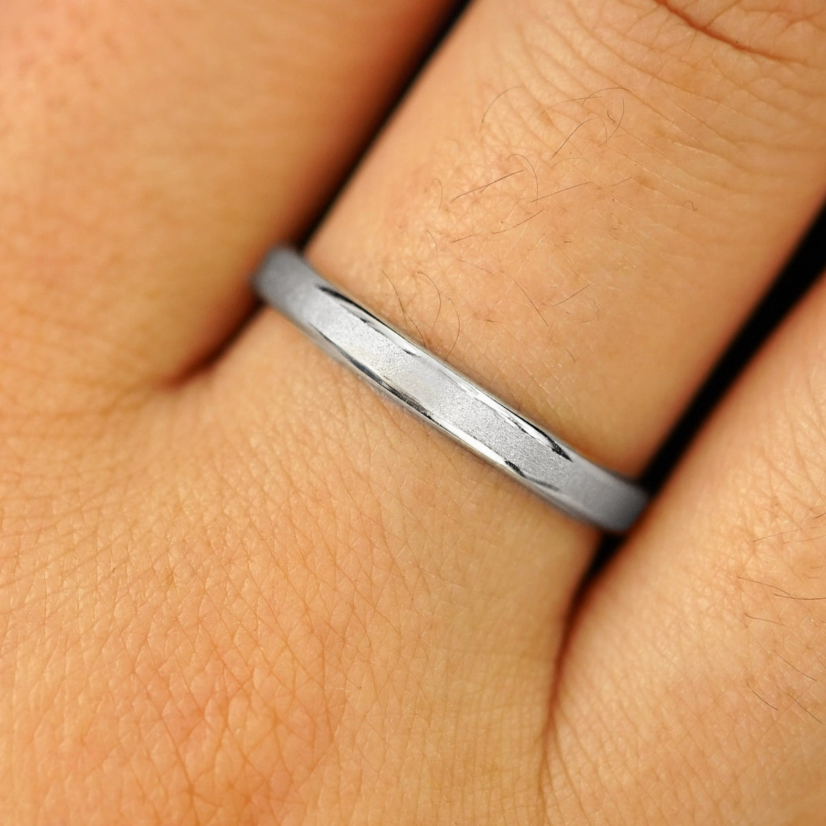 Close up view of a model's hand wearing a solid platinum Beveled Edge Band