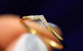 Cloe up view of a yellow gold chevron diamond band held between a models fingers