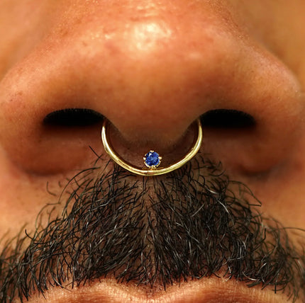 Close up view of a model's nose wearing a 14k yellow gold sapphire Raised Gemstone Septum