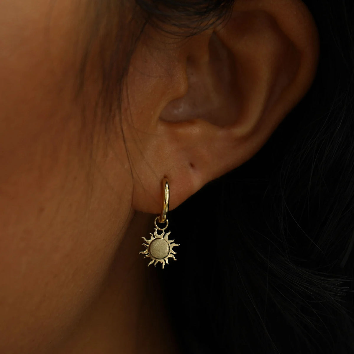 Close up view of a model's ear wearing a champagne gold Sun Charm on a Curvy Huggie Hoop