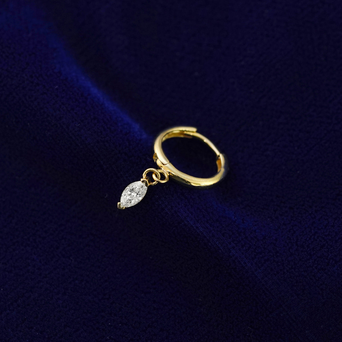 A recycled solid 14k gold Marquise Lab Diamond Dangle Huggie Hoop earring on a dark blue background
