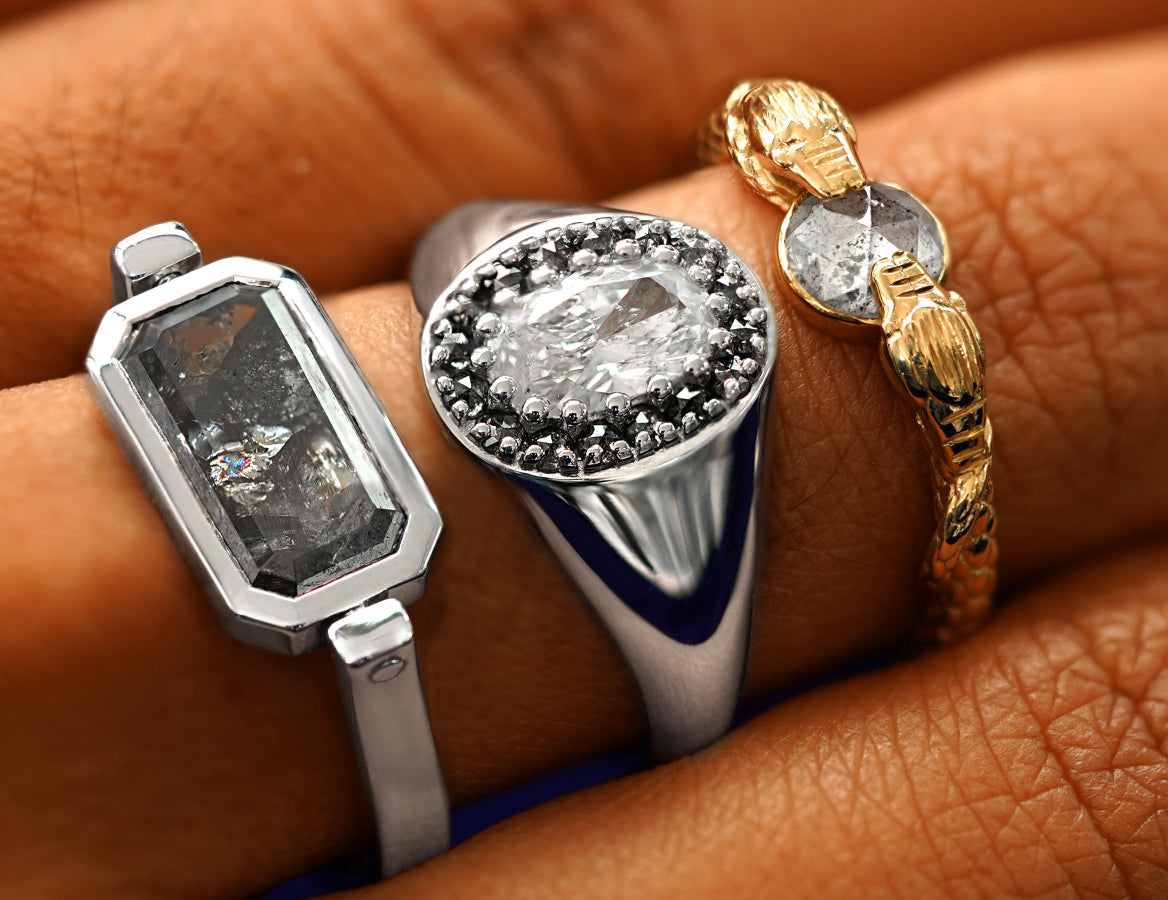 A model's finger wearing a Diamond Spinner Ring,  Platinum Diamond Signet, and a Guardian Snakes Ring stacked