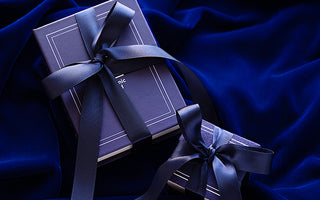 An Automic Gold Ring Box and Book Box both gift wrapped in a blue ribbon