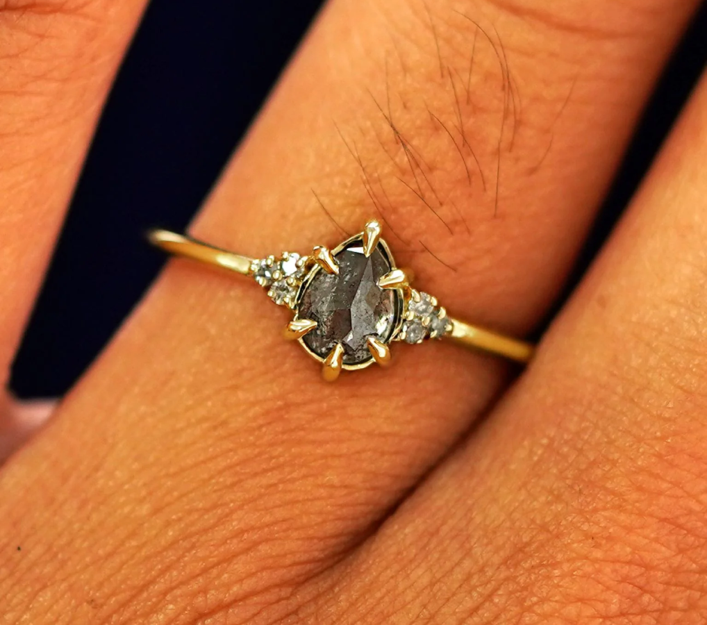 Close up view of a model's fingers wearing a 14k yellow gold Pear Salt and Pepper Diamond Cluster Ring