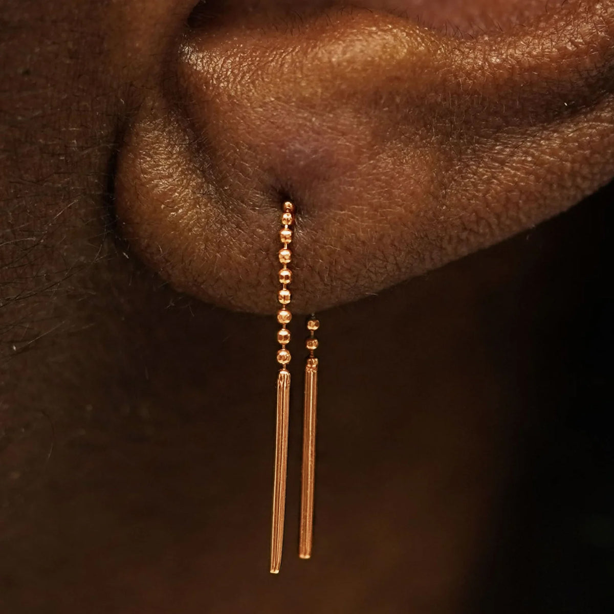 Close up view of a model's ear wearing a solid 14k rose gold Mini Threader