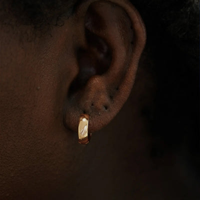 Close up view of a model's ear wearing a 14k rose gold Medium Wide Huggie Hoop Earring