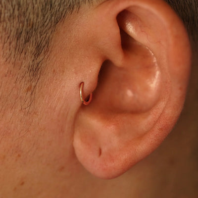 A model's ear wearing a 14k rose gold Mini Seamless Huggie Hoop in a tragus piercing