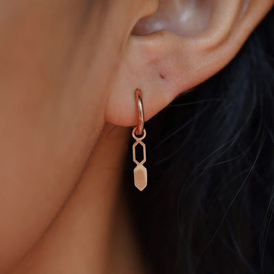 Close up view of a model's ear wearing a rose gold Tanlah Charm on a Curvy Huggie Hoop