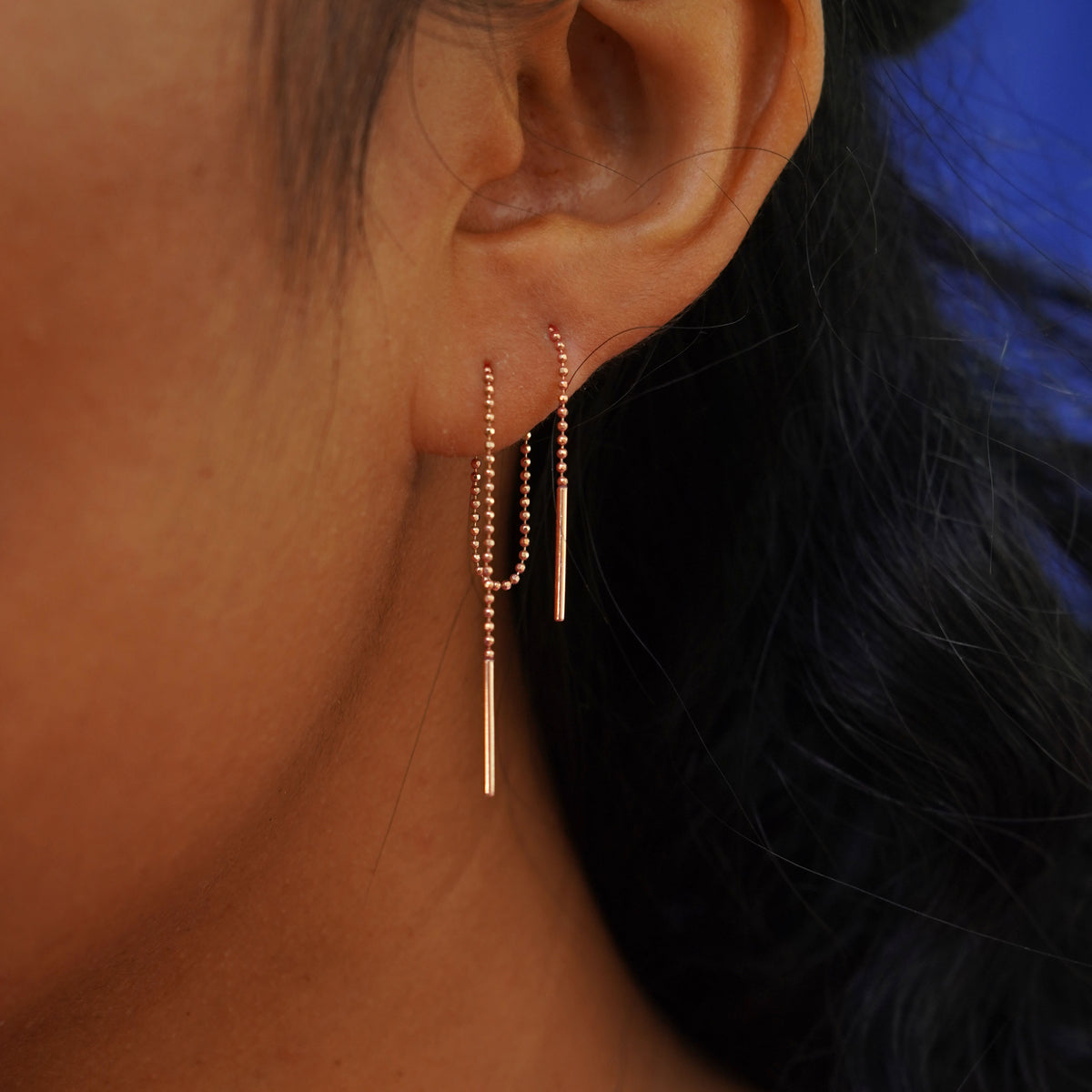 Close up view of a model's ear wearing a rose gold Threader through two piercings to create a loop behind their ear