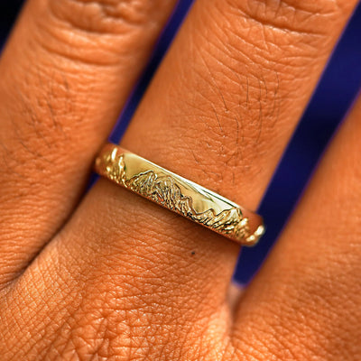 Close up view of a model's fingers wearing a 14k yellow gold Mountains Band