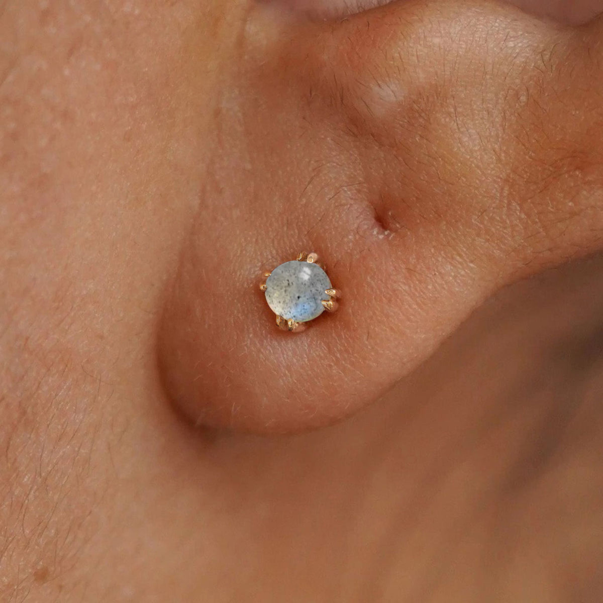 Close up view of a model's ear wearing a yellow gold labradorite earring