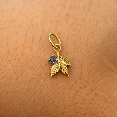 A solid 14k yellow gold alexandrite Gemstone 3 Leaves Charm resting on the back of a model's hand