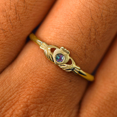 Close up view of a model's fingers wearing a 14k yellow gold alexandrite Thin Gemstone Claddagh Ring
