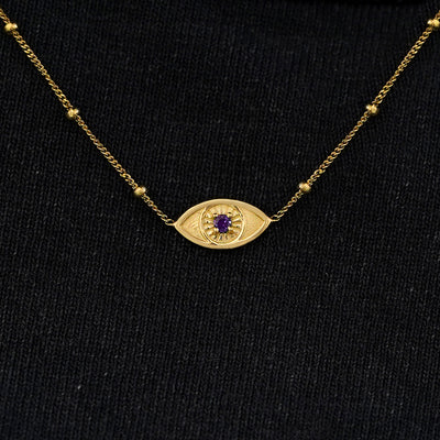 Close up view of a solid 14k yellow gold amethyst evil eye necklace against a model's black shirt
