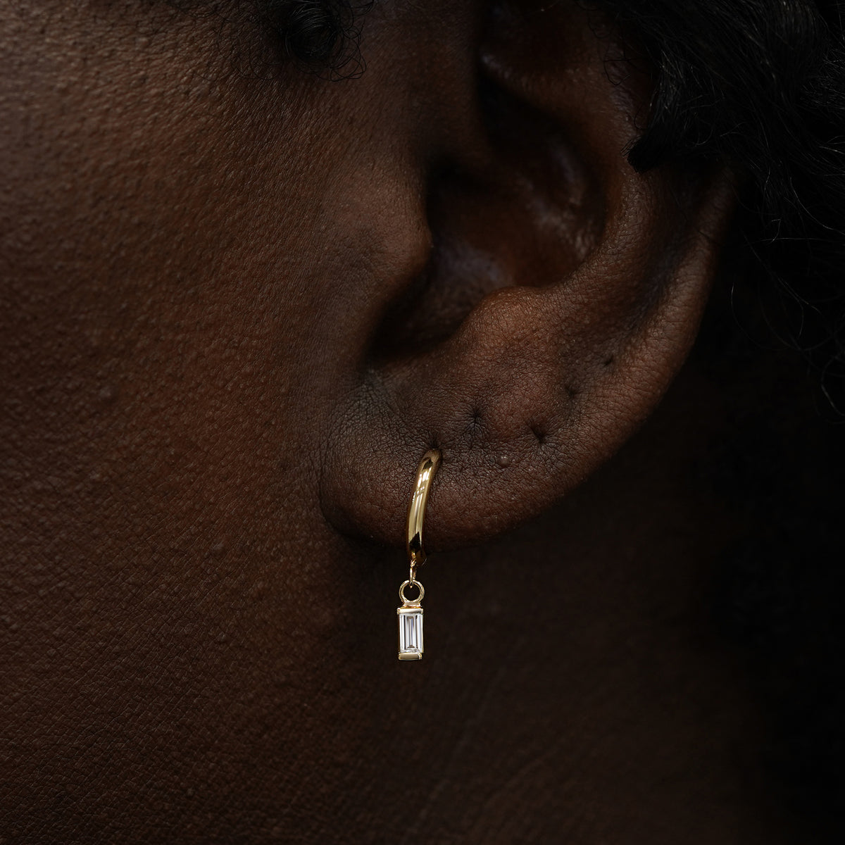 A model wearing a solid 14k gold baguette clear diamond charm hoop earring