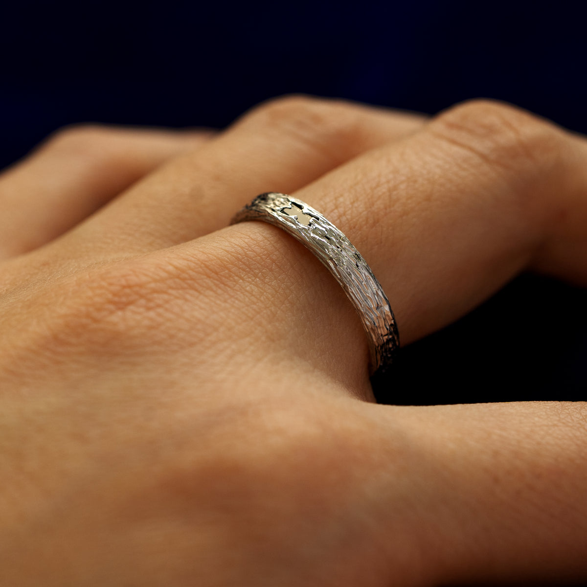Side view of a models finger wearing a black baguette diamond raw band to show the details of the ring finish