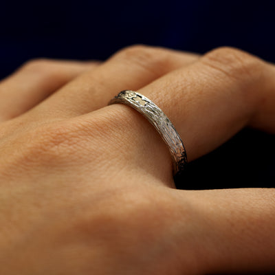 Side view of a models finger wearing a black baguette diamond raw band to show the details of the ring finish