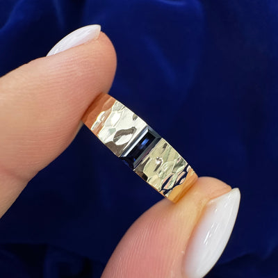 A model is holding 14k Yellow Gold 5x2.5mm Baguette Lab Sapphire on 5mm Hammered Industrial Band Custom Ring