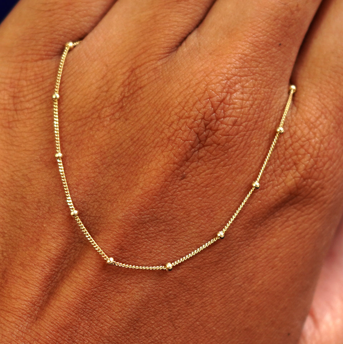 A solid gold Beaded Essential Chain resting on the back of a model's hand