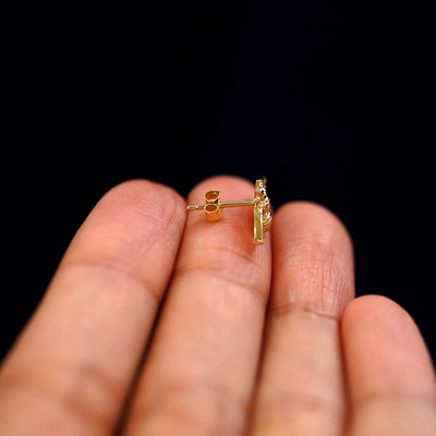 A 14k gold Bee Earring sitting sideways on a model's fingertips to show detail