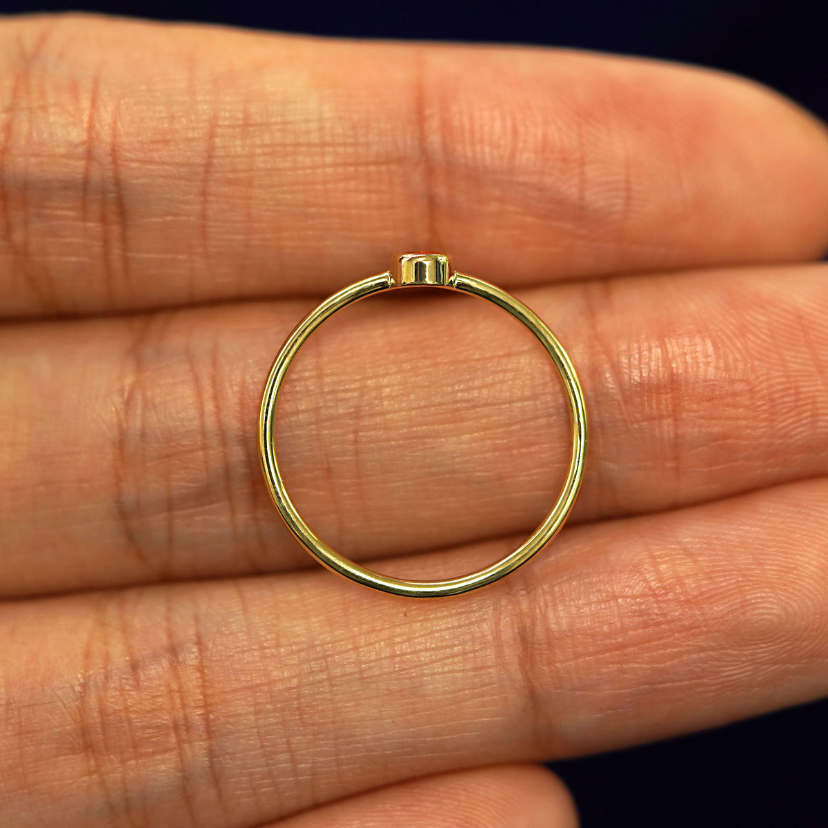 A yellow gold Fire Opal Ring in a model's palm showing the thickness of the band