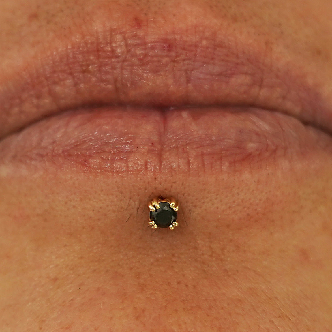 Close up view of a model's lips wearing a 14k yellow gold Black Diamond Flatback in a labret piercing