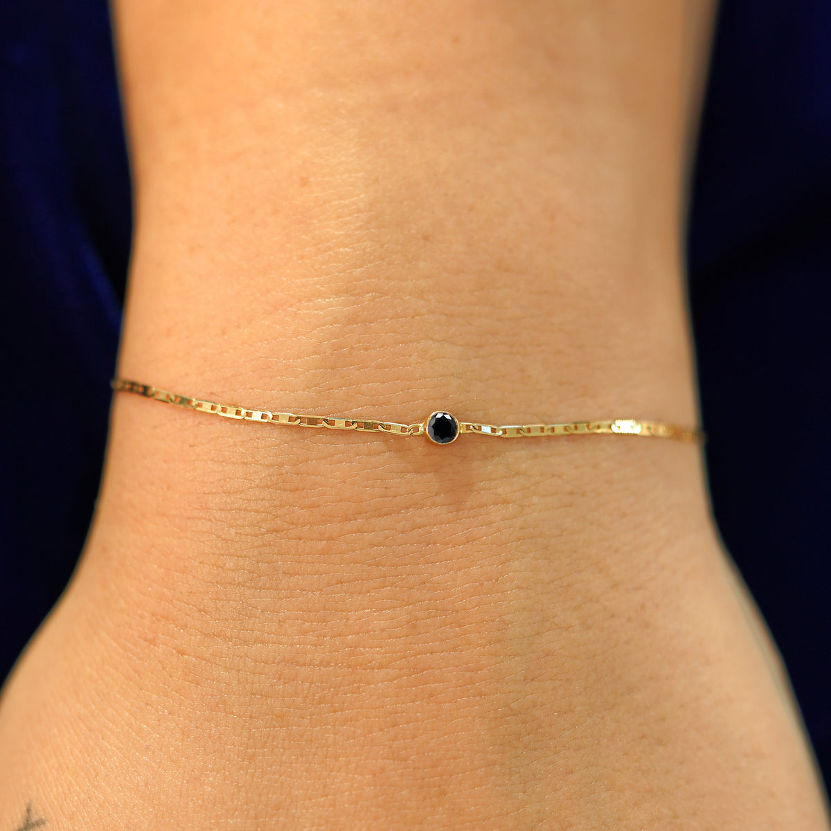 A model's wrist wearing a solid 14k yellow gold Black Diamond Bracelet