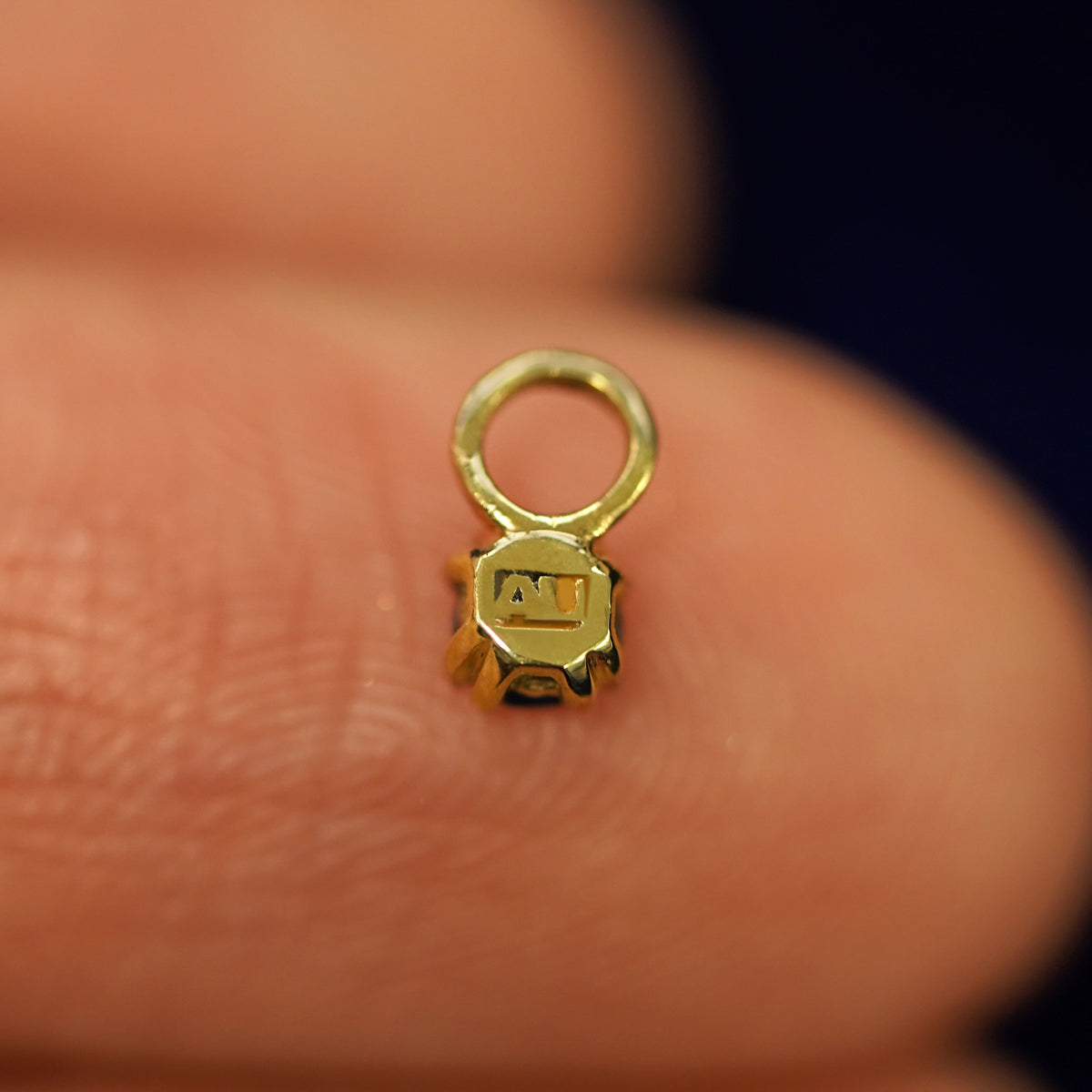 A solid gold Black Diamond Charm for earring facedown on a model's fingertip to show the solid back of the charm