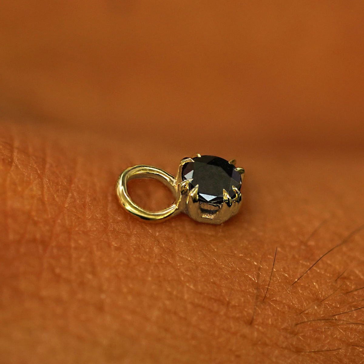 A solid yellow gold Black Diamond Charm for earring resting on the back of a model's hand