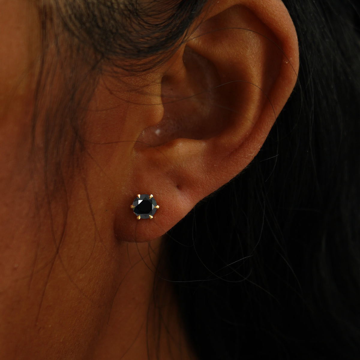 A model's ear wearing a 14k yellow gold black 5mm Moissanite Earring