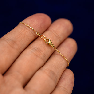 A block initial bracelet on a models fingertips to show the lobster claw clasp on the cable chain