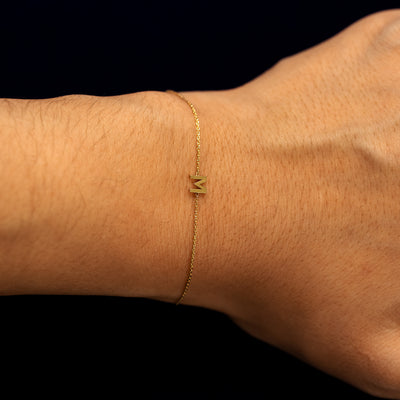A models wrist wearing a solid gold block initial letter M bracelet