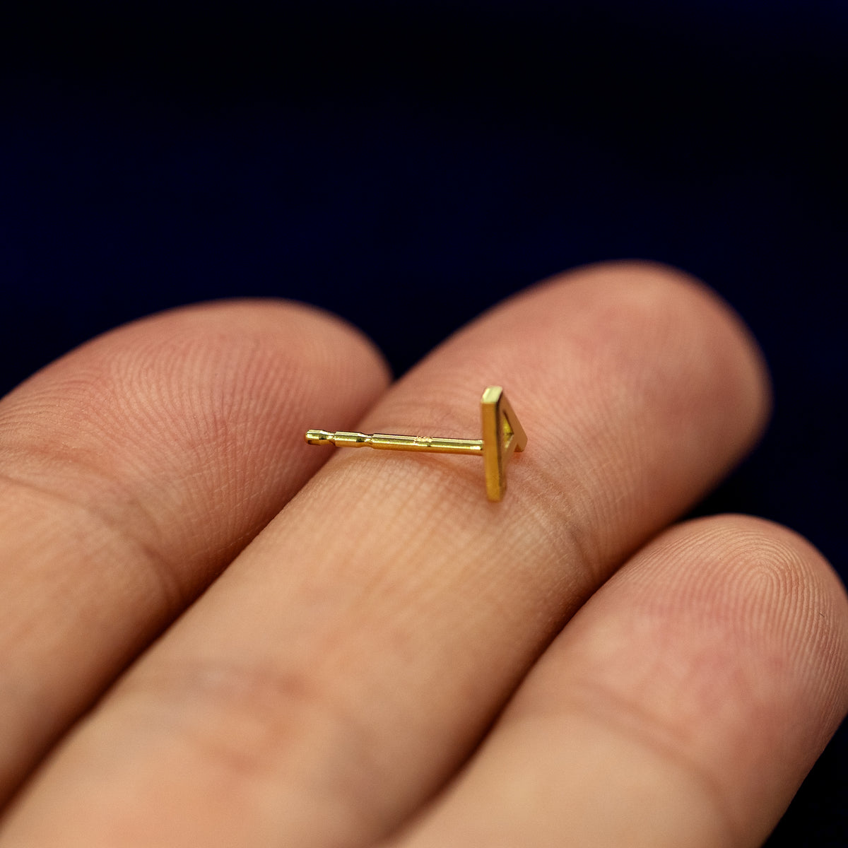 A 14k gold letter A Block Initial Earring resting sideways on a model's fingertip to show the pushback post without a backing