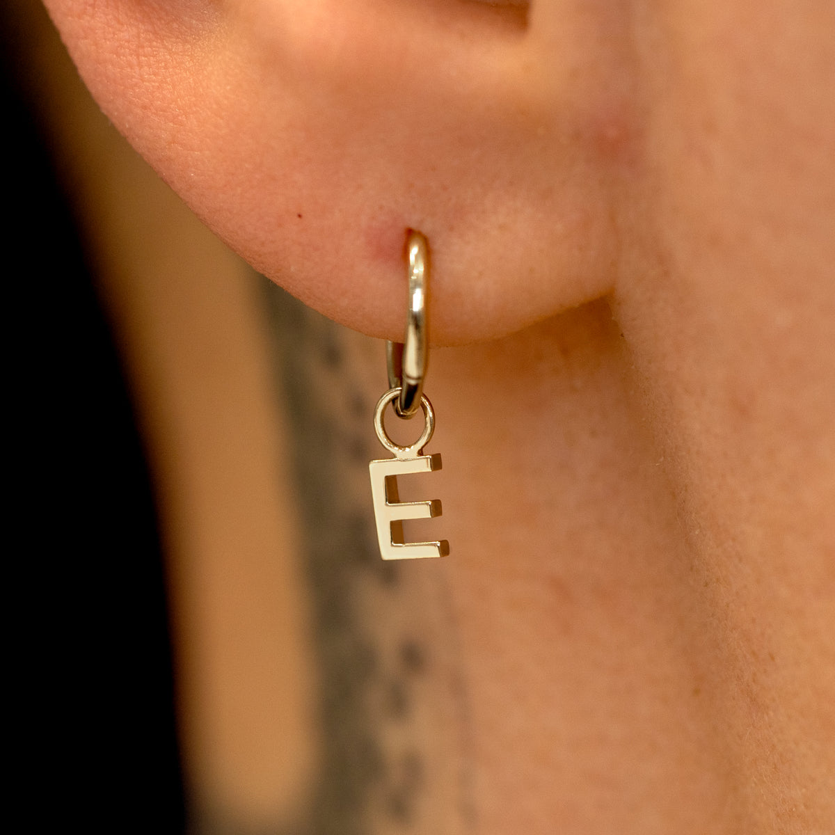 Close up view of a model's ear wearing a 14k champagne gold Seamless Huggie Hoop with a letter E block initial charm