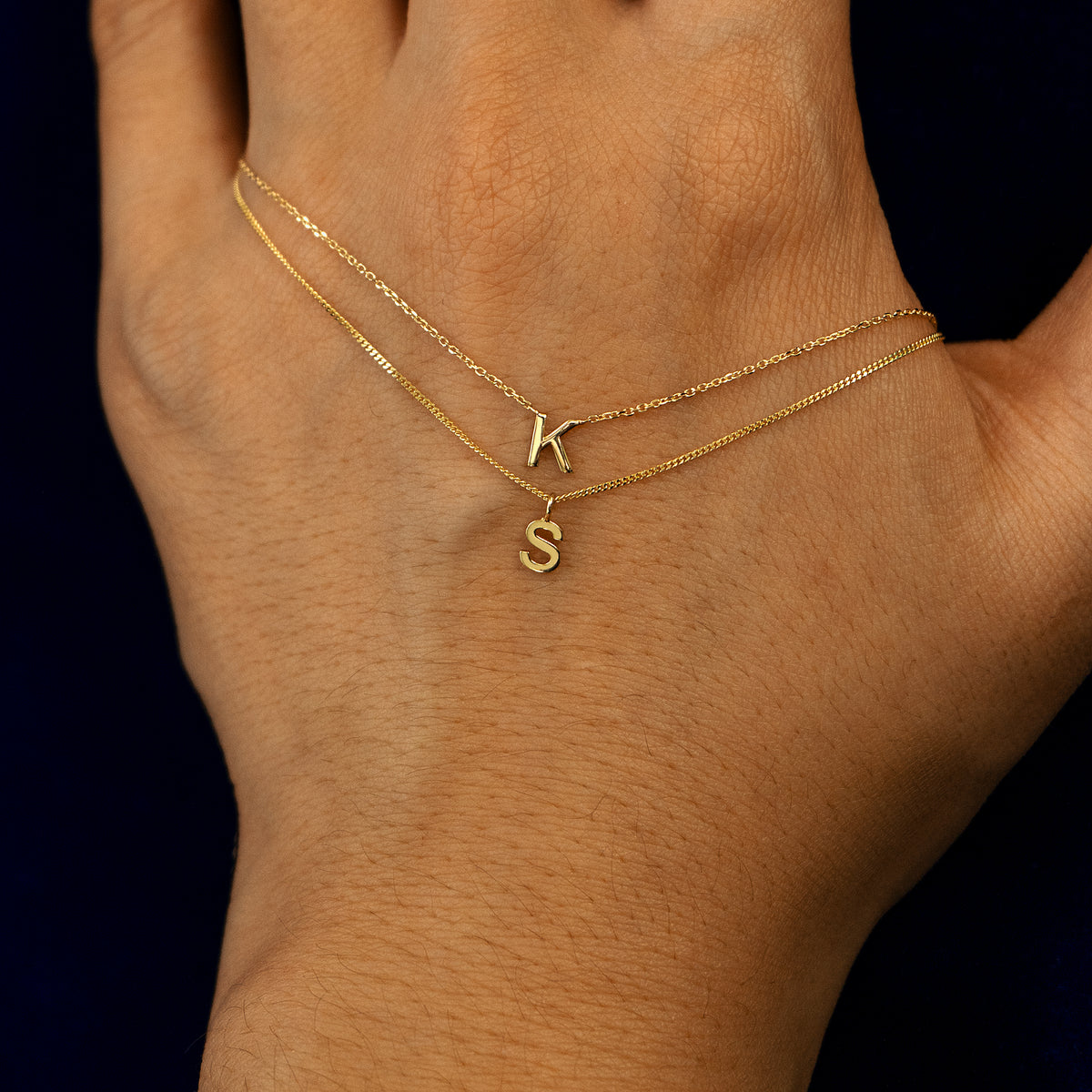 A model holding a block initial necklace and a block initial charm necklace layered