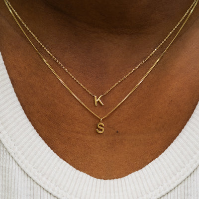 A model wearing a block initial necklace and a block initial charm necklace layered