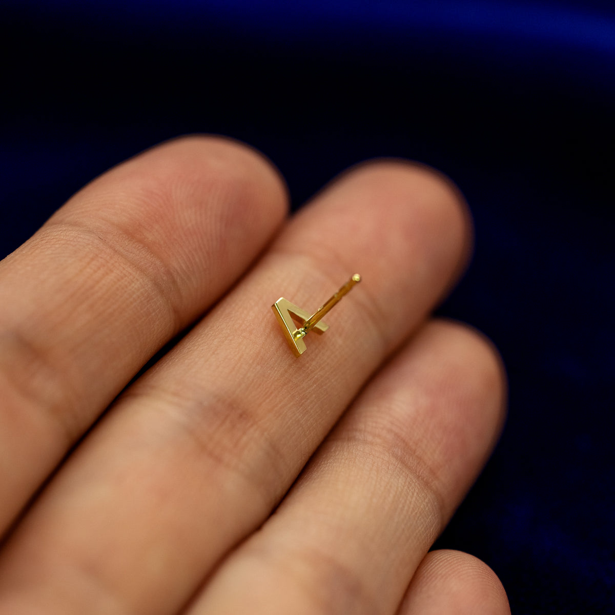 A solid 14k gold Block Initial Earring in the letter A laying face down on a model's fingertip to show the underside of the initial