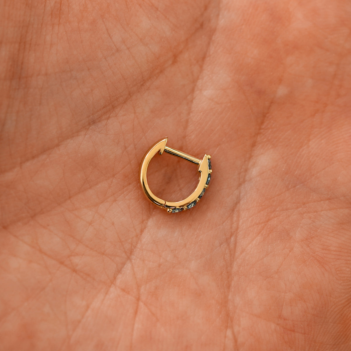 A closed blue sapphire huggie hoop laying in a models palm