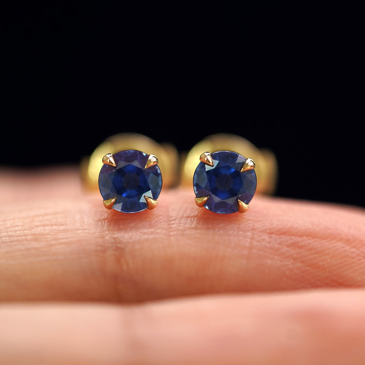 A pair of solid yellow gold Blue Sapphire Pressure Lock Earrings resting on a model's fingertip