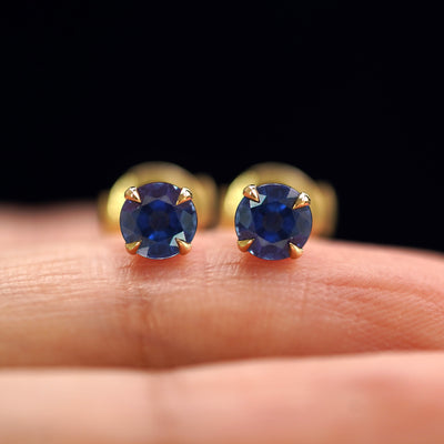 A pair of solid yellow gold Blue Sapphire Pressure Lock Earrings resting on a model's fingertip