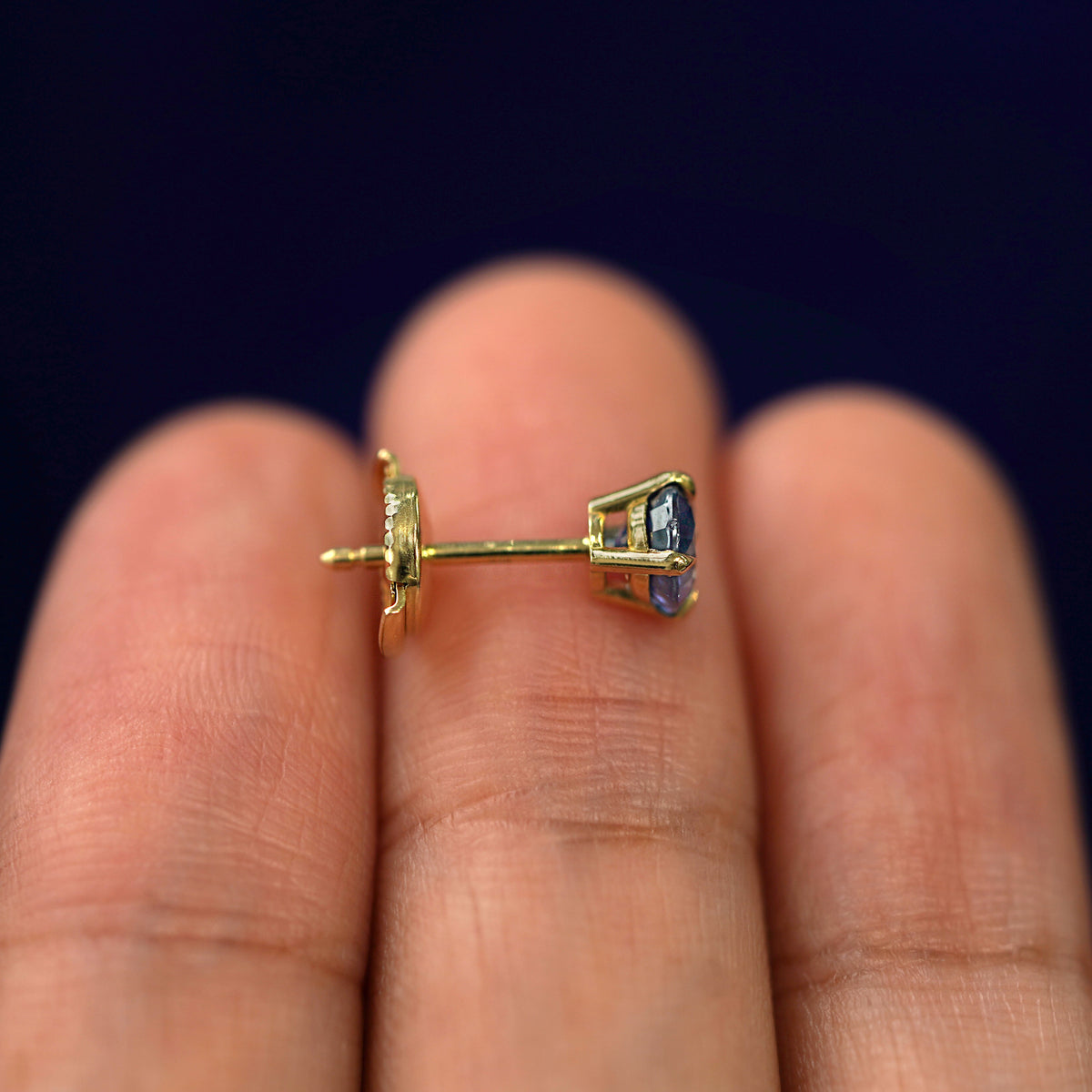 A 14k gold Blue Sapphire Pressure Lock Earring resting sideways on a model's fingertips to show detail