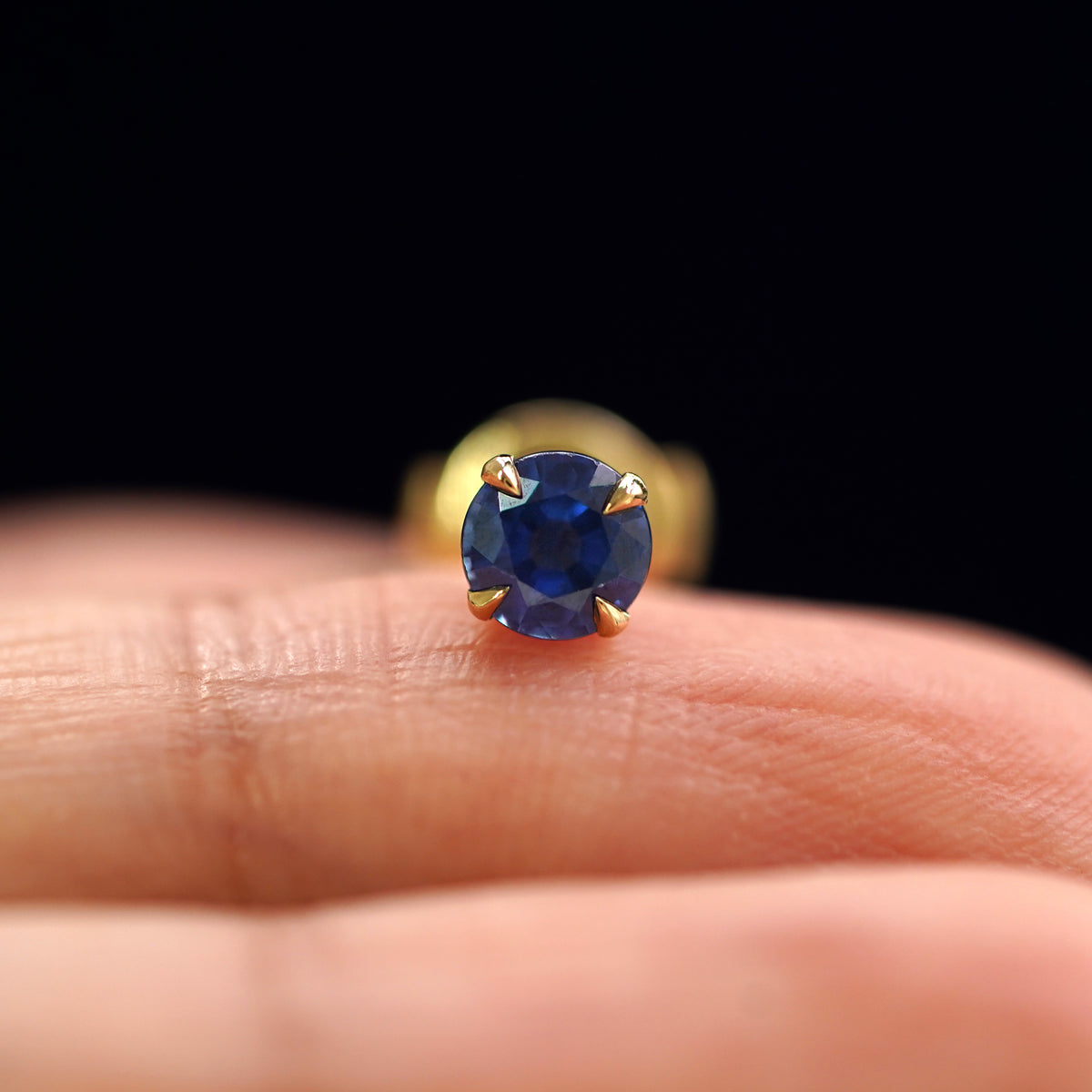 A 14k yellow gold Blue Sapphire Pressure Lock Earring resting on a model's fingertip