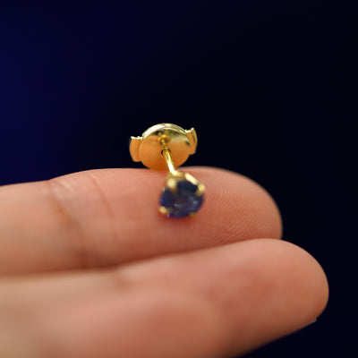A solid gold Blue Sapphire Pressure Lock Earring tilted on a model's fingertip to show the pressure lock backing on the post