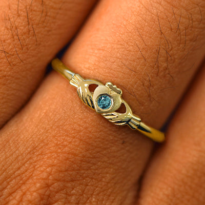 Close up view of a model's fingers wearing a 14k yellow gold blue topaz Thin Gemstone Claddagh Ring