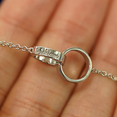 A white gold Bound Together Bracelet laid across a model's fingers to show the engraving of a name on one of the rings