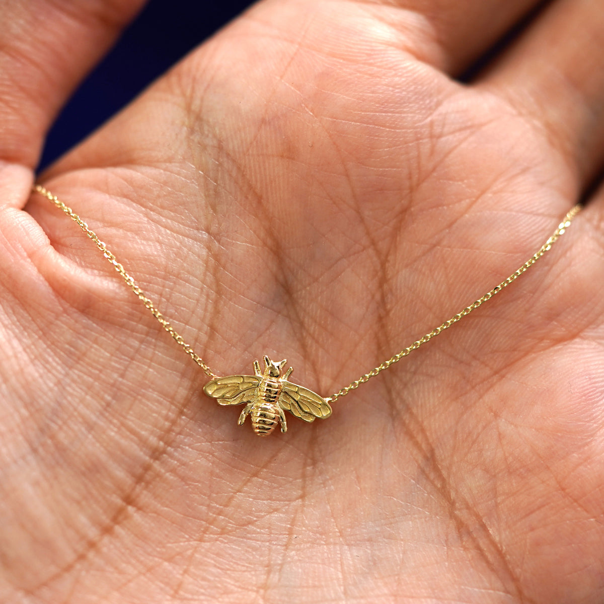 A yellow gold Bee Necklace draped on a model's palm