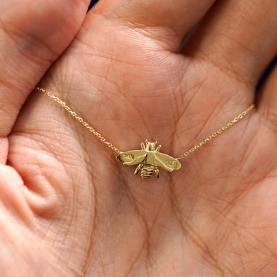 A model's hand holding a yellow gold Bee Necklace showing the underside view and the metal stamps