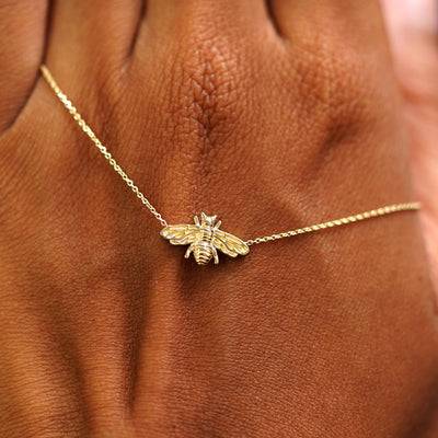 A solid gold Bee Necklace resting on the back of a model's hand
